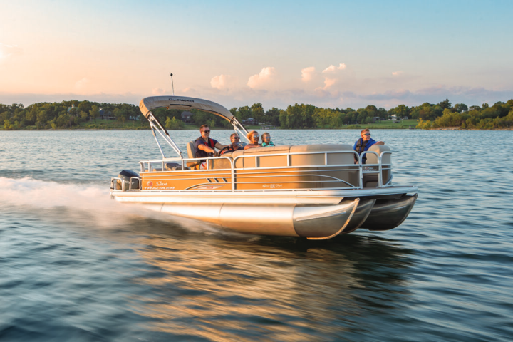 Pontoon boat with people cruising on a lake during sunset.