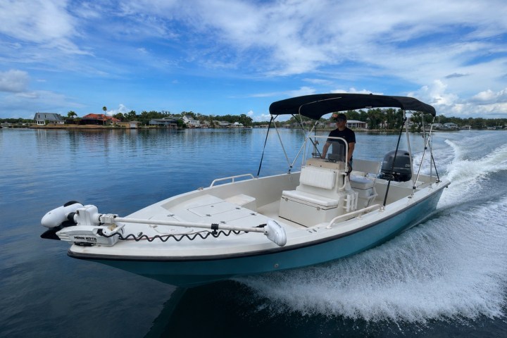 Man steering a motorboat speeding across calm water under a blue sky.